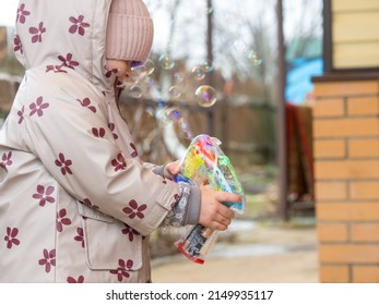 A Small Child Blows Soap Bubbles From A Gun