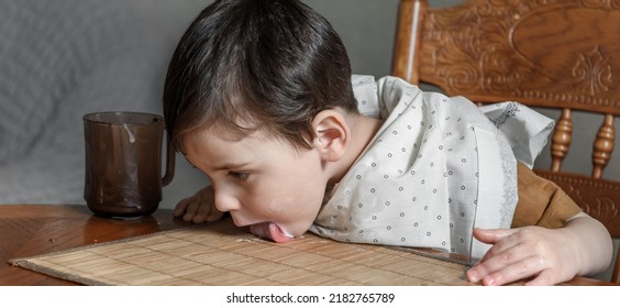 A Small Child Boy Licks Food Off The Table