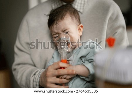 Small child coughs and wheezes while holding nebulizer mask as parent holds them close in home setting