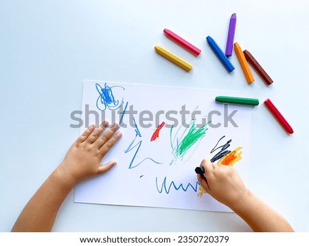 small child draws with pastel crayons on white table.