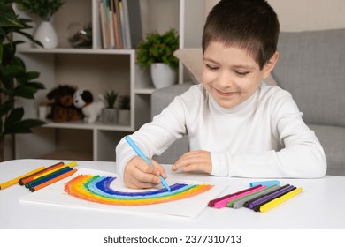 A small child draws a rainbow with felt-tip pens in a sketchbook while sitting at a table - Powered by Shutterstock