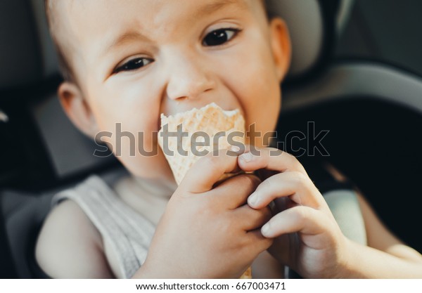 A small child eating ice cream, sitting strapped in\
the car seat