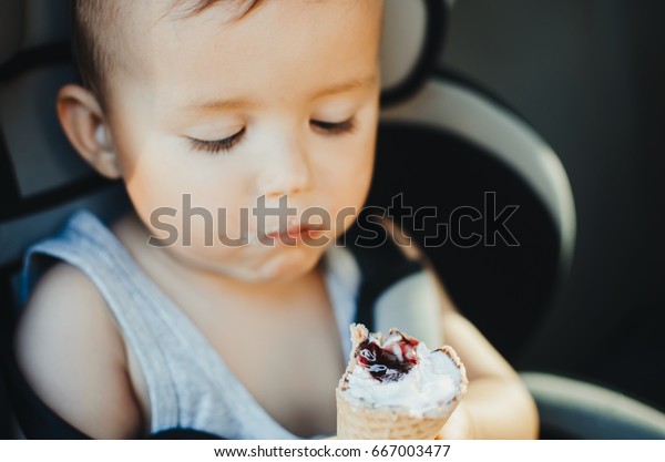 A small child eating ice cream, sitting strapped in\
the car seat
