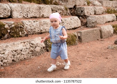 A Small Child, A Girl, Walking Outdoors, In The Afternoon, On The Background Of A Stone Staircase