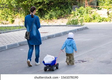 A Small Child Helps Her Mother Carry A Heavy Bag, Carrying It In Her Toy Car.