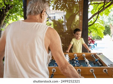 Small child and his grandfather sharing a multigenerational moment playing foosball together. - Powered by Shutterstock