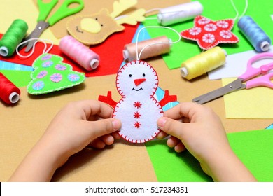 Small Child Holding A Felt Christmas Snowman In Hands. Little Kid Shows Christmas Ornament Crafts. Workplace In Kindergarten, School Or Home. Kids Christmas Crafts Idea. Children Winter Creativity