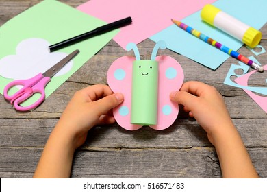 Small child holding paper butterfly in his hands. Child shows paper cut art crafts. Funny butterfly made of colored paper. Office supplies on a wooden table. Children creativity and craft art workshop - Powered by Shutterstock