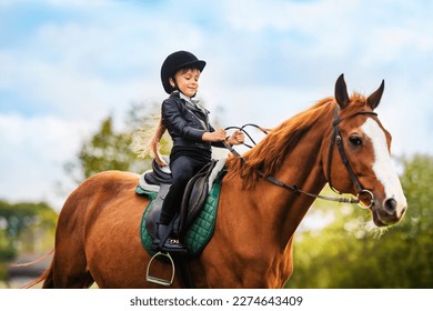 Small child in jockey outfit is riding horse on blue sky with clouds background. School of riding and equestrian sports. - Shutterstock ID 2274643409