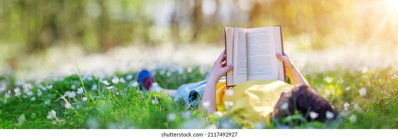 Small child lying down on the field in the spring park and reading a book. Concept of studying, learning and interesting of the literature. - Powered by Shutterstock