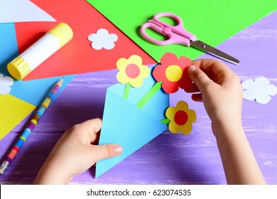 Small child makes paper crafts for mother's day or birthday. Small child doing paper flowers for mom. Simple nice kids gift idea to mom. Scissors, glue stick, flowers templates, pencil on a wood table