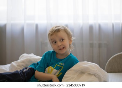 A Small Child On The Bed Builds A Funny Grimace, A Sly Look.