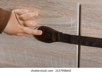 A Small Child Opens A Chest Of Drawers Wardrobe With Child Protection. Dangerous Situation At Home. Child Trapped Finger In The Door.