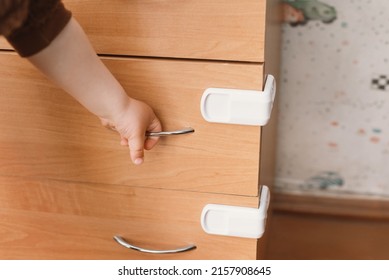 A Small Child Opens A Chest Of Drawers Wardrobe With Child Protection. Dangerous Situation At Home. Child Trapped Finger In The Door.