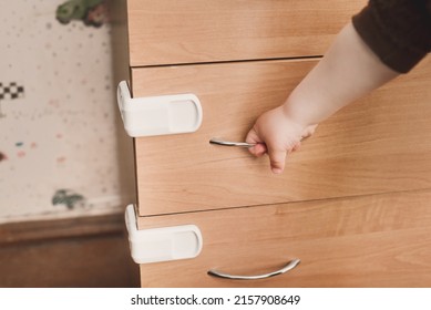 A Small Child Opens A Chest Of Drawers Wardrobe With Child Protection. Dangerous Situation At Home. Child Trapped Finger In The Door.