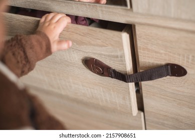 A Small Child Opens A Chest Of Drawers Wardrobe With Child Protection. Dangerous Situation At Home. Child Trapped Finger In The Door.