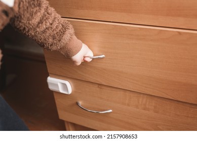 A Small Child Opens A Chest Of Drawers Wardrobe With Child Protection. Dangerous Situation At Home. Child Trapped Finger In The Door.