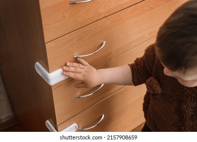 A Small Child Opens A Chest Of Drawers Wardrobe With Child Protection. Dangerous Situation At Home. Child Trapped Finger In The Door.