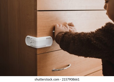 A Small Child Opens A Chest Of Drawers Wardrobe With Child Protection. Dangerous Situation At Home. Child Trapped Finger In The Door.