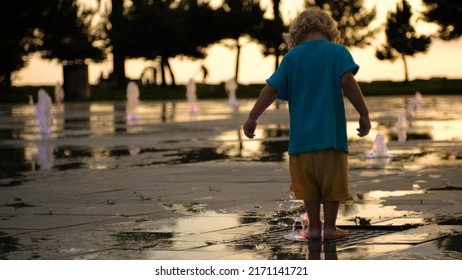 a small child outdoors playing with water from a ground fountain at sunset