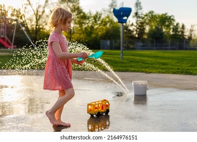 Small Child Playing With Outdoor Toys At Splash Pad Playground In Summer. Water Park With Fountains For Children. Summertime Activities For Kids