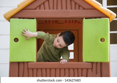 Small Child Playing With Window In A Toy Playhouse In An Yard Or An Outdoor Playground.