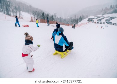 Small child pushes his father on a sled down a snowy hill and looks after him. Back view - Powered by Shutterstock