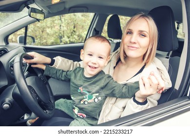 A Small Child Sits In His Mother's Arms Holding The Steering Wheel. Children In The Car. Love Little Boys Machines