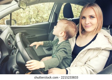 A Small Child Sits In His Mother's Arms Holding The Steering Wheel. Children In The Car. Love Little Boys Machines