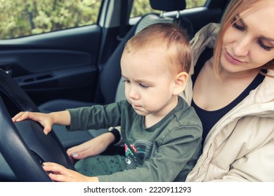 A Small Child Sits In His Mother's Arms Holding The Steering Wheel. Children In The Car. Love Little Boys Machines