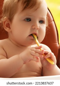 Small Child Sits On A Chair And Eating With Spoon. Little Smiling Girl Sits In Baby-chair And Have A Breakfast. Baby With Big Eyes And Red Curly Hair Eats At A Table. Summer Vacation Concept