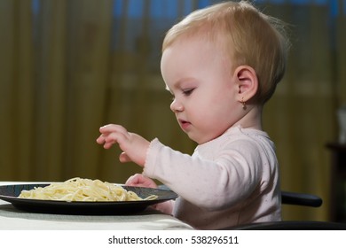 The Small Child Sits At A Table And Eating Pasta