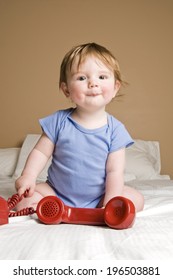 A Small Child Sitting On The Bed With A Red Phone.