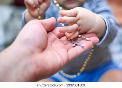 A small child takes a rosary from his dad's hand