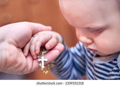 A Small Child Takes A Rosary From His Dad's Hand