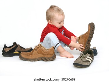 Small Child Tries To Put On His Father's Shoes. Baby Boy With Big Shoes In Hand Isolated On White.