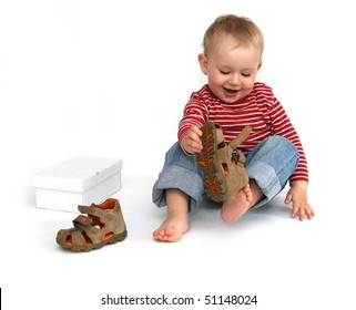 Small child tries to put on his shoes. Baby boy with summer shoes in hand isolated on white.