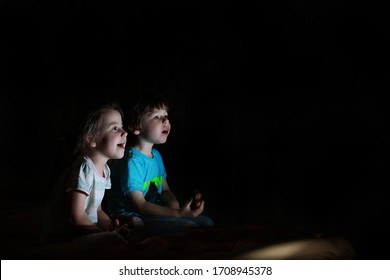 Small Children In A Dark Room Watching TV At Night.
