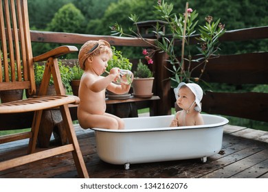 Small Children With A Drink Sitting In Bath Outdoors In Garden In Summer.