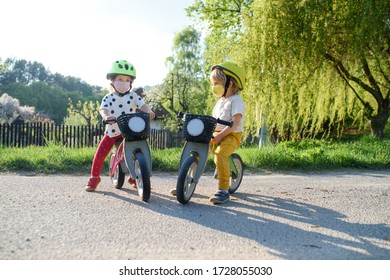 Small Children With Face Masks Playing Outdoors With Bike, Coronavirus Concept.