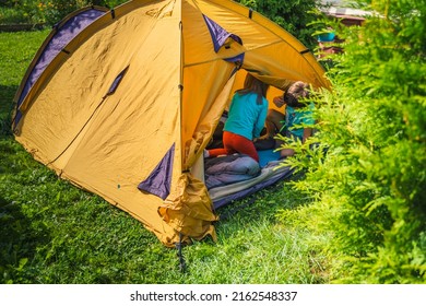 Small Children, Kids Play, Read In Orange Tourist Tent. Family Trip, Hike To Nature. Backyard Games, Having Fun. Outdoor Recreation, Activity. Self-assembly, Setting Up Camping Tent On Lawn, Grass.