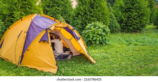 Small Children, Kids Play, Read In Orange Tourist Tent. Family Trip, Hike To Nature. Backyard Games, Having Fun. Outdoor Recreation, Activity. Self-assembly, Setting Up Camping Tent On Lawn, Grass.