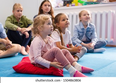 Small Children Sitting On The Floor Listening Attentively To The Teacher In Kindergarten In Preschool