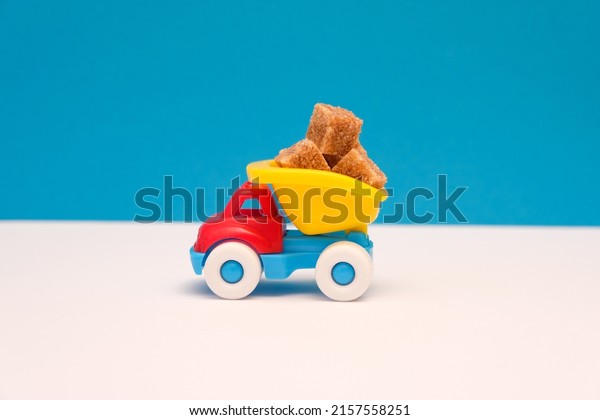Small children\'s truck transports brown sugar\
cubes; white and blue paper\
background