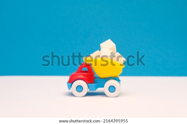 Small children\'s truck transports white sugar\
cubes; white and blue paper\
background