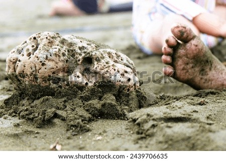 a small child's feet are filled with sand on the beach and next to it there is a unique coral rock.