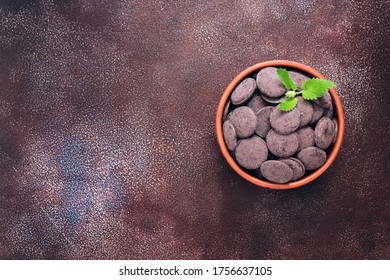 Small chocolate button with mint leaf s bowl on a dark brown rustic background. Top view, copy space