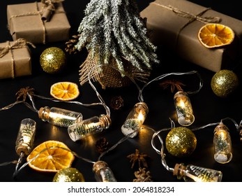 Small Christmas tree on a black background. Glowing lights decorating glass jars with corks, inside are small green Christmas trees on artificial snow. Gift box, cones and balloons. Christmas composit - Powered by Shutterstock