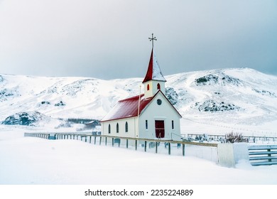 Small church with bright red roof stands in contrast to snow covered field and mountains in a small village in Iceland.  Church buildings like this are common in many of Iceland's small villages. - Powered by Shutterstock