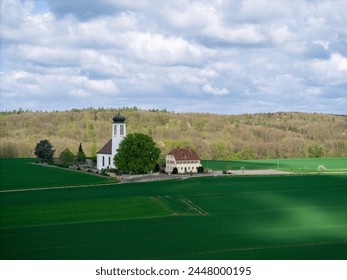 Small church with cemetery in the middle of blooming fruit trees and fields captured with a drone in spring